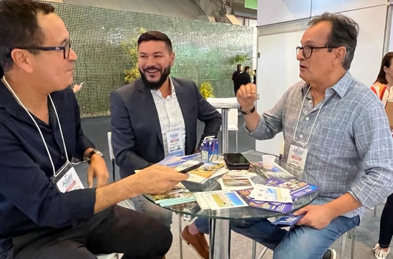 Três homens sentados em mesa de reunião